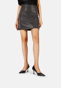 Mini gonna nera in metallo con superficie testurizzata e design aderente. Indossata con tacchi neri a punta, che mettono in risalto una silhouette snella.