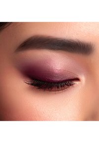 Primo piano di un occhio con trucco borgogna intenso, sfumato con leggeri riflessi luminosi, ciglia nere folte e una pelle liscia e uniforme.