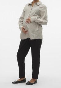 Striped button-up shirt in light beige with dark stripes, paired with black trousers. Model holds belly, wearing black flats; relaxed fit.