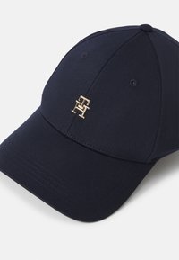 Navy baseball cap made of smooth fabric with a curved brim. Features a gold embroidered logo on the front. Spot for ventilation eyelets.