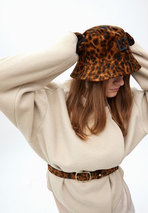 Leopard print bucket hat in plush material with a black logo detail, worn with a cream oversized sweater and matching belt.