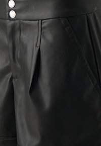 Černé šortky z imitace kůže s vysokým pasem, sklady na přední straně a dvěma bočními kapsami. Dokončeno stříbrnými kovovými knoflíky v pase.