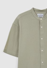 Camicia verde chiaro a maniche corte con colletto rotondo, chiusura a bottoni e tessuto morbido e testurizzato, con dettagli di cucitura sottili.