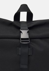 Black fabric bag with a textured surface, featuring a black buckle closure and strap. The design includes a top handle for carrying.
