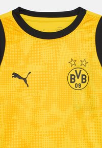 Gul sportstrøye med svarte detaljer, har en prikkete tekstur, Puma-logo og BVB 09-emblem med to stjerner over.