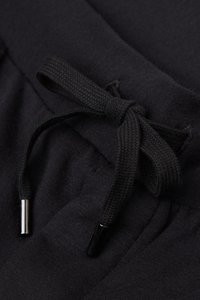 Svarta svettbyxor har en strukturerad tyg, ett elastiskt midjeband och en dragsko med svarta metallaglar.