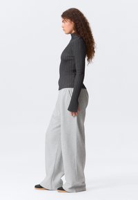 Μαύρο ριγέ ζιβάγκο με μακριά μανίκια σε συνδυασμό με ανοιχτό γκρι φαρδιά φούτερ παντελόνια. Λείες υφές, άνετη εφαρμογή και μινιμαλιστικός σχεδιασμός.