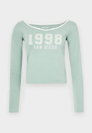 Piparmētru zaļš garām piedurknēm crop tops, kuram ir plecus atklājošs dekoltē un uz krūtīm balts uzdrukāts teksts "1998 SAN DIEGO". Mīksta auduma.