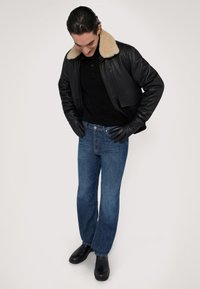 Svart läderbomberjacka med en tan pälskrage, svarta handskar, svart polo-tröja och blå raka jeans, i kombination med svarta stövlar.