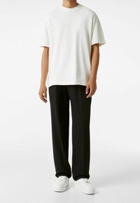 Camiseta blanca de manga corta con cuello redondo, combinada con pantalones negros y zapatillas blancas. Ajuste sencillo y relajado con textura suave.