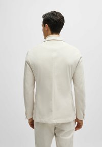Blazer ajusté beige clair avec une finition texturée, design à bouton unique, revers en pointe et trois boutons sur chaque manche.