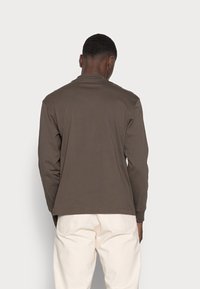 Långärmad brun skjorta i mjukt tyg, med en enkel rund hals och lös passform, tillsammans med ljusa byxor.