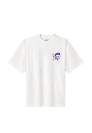 T-shirt blanc à manches courtes avec un petit motif bleu et rouge d’un visage souriant tenant un autocollant Vans près de la poitrine.