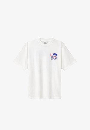 T-shirt blanc à manches courtes avec un petit motif bleu et rouge d’un visage souriant tenant un autocollant Vans près de la poitrine.