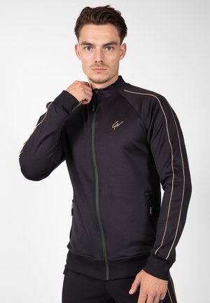 Black athletic zip-up jacket with gold accents, featuring side pockets, a high collar, and a fitted design. Smooth texture.