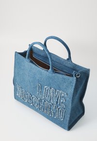 Denim tote bag med texten "LOVE MOSCHINO" i vit broderi. Har dubbla handtag, dragkedjestängning och en brun innerfoder.