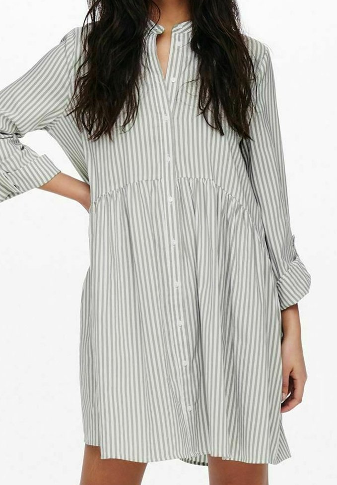 Pasiasta sukienka koszulowa w jasnoszarym i białym kolorze, z kołnierzykiem, długimi rękawami i marszczonym paskiem w talii. Gładka tekstura tkaniny.