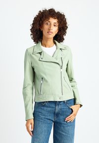 Miętowa zielona skórzana kurtka motocyklowa ze srebrnymi zamkami i zatrzaskami. Posiada klasyczny kołnierz i dopasowany krój, zestawiona z jeansami z wysokim stanem.