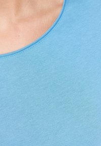 Svetle modré tričko s krátkým rukávem a kulatým výstřihem; vyrobené z jemné, hladké látky, s jednobarevným povrchem a bez viditelných vzorů.