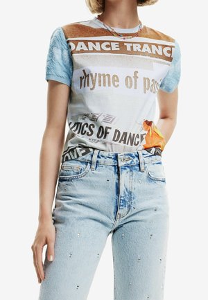 Persona que lleva una camiseta gráfica multicolor con texto y vaqueros azul claro adornados con pequeñas piedras de strass.
