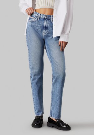 Jeans de tiro alto en un azul claro, con corte recto, textura desvanecida y diseño de cinco bolsillos, combinados con unos mocasines negros y un suéter corto.