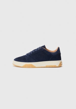 Mörkblå sneakers med texturerad logotyp på sidan, beige stoppad krage, krämfärgad mellansula och ljusbrun gummisula.