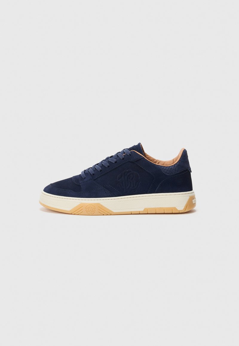 Navy blue sneaker with textured logo on side, beige cushioned collar, cream midsole, and light brown rubber outsole.