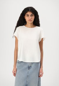 Top bianco a maniche corte realizzato in tessuto leggero, con scollo rotondo e texture leggermente stropicciata, abbinato a una gonna di jeans.
