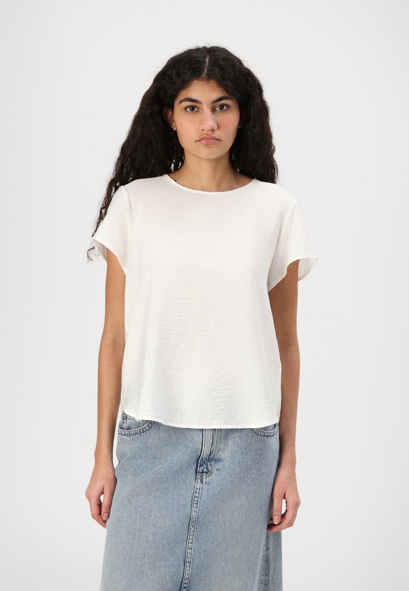 Top bianco a maniche corte realizzato in tessuto leggero, con scollo rotondo e texture leggermente stropicciata, abbinato a una gonna di jeans.