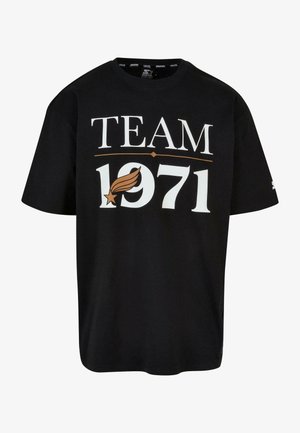 Must märgiga must puuvillane T-särk, millel on suur valge ja kuldne "TEAM 1971" graafika koos tähe ja tiibade disainiga. Lühikesed varrukad ja mugav lõige.