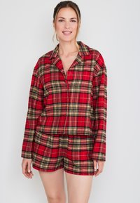 Rood geruite pyjama set van zacht materiaal; bevat een knoopsluiting shirt met lange mouwen en bijpassende shorts. Inclusief zwarte en beige accenten.