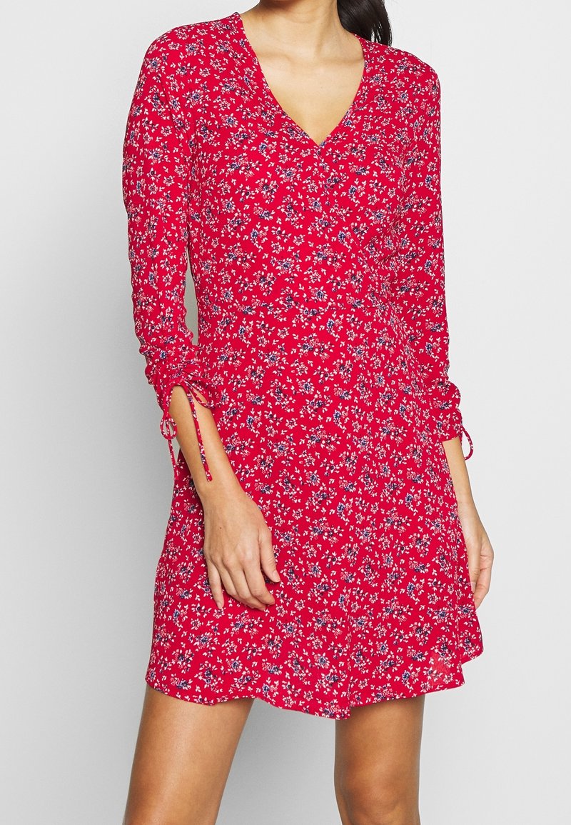 Rotes Blumenkleid mit langen Ärmeln, Wickeldesign und Raffung an den Bündchen. Aus leichtem, strukturiertem Stoff mit kleinen blauen Blumen.
