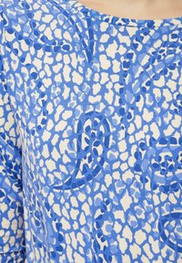 Blauwe gemusterde stof met onregelmatige vormen in verschillende tinten blauw op een crème achtergrond; gladde textuur, lichtgewicht ontwerp.