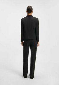 Zwart pak met een getailleerde blazer en bijpassende broek, met een strak ontwerp, een gladde textuur en zonder zichtbare patronen of accenten.