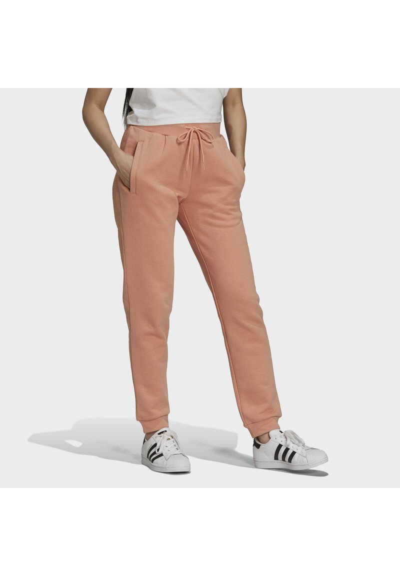 Joggers de algodón color durazno con cintura elástica, detalle de cordón, bolsillos laterales y piernas ajustadas. Combinados con zapatillas blancas con rayas negras.