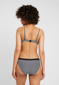 Conjunto de bikini com padrão em preto e branco, com alças ajustáveis, apresentando um fecho de gancho e um corte clássico na parte de baixo. Textura de tecido suave.