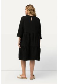 Vestito nero a balze con maniche a tre quarti, tessuto testurizzato, dettaglio con apertura a chiave sul retro e vestibilità comoda, abbinato a sandali leggeri e piatti.