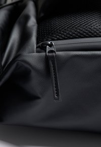 Czarna torba z textured materiału, posiadająca kieszeń na zamek, siateczkowe detale oraz elegancki czarny suwak z skórzanym akcentem.