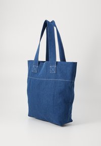 Blaue Denim-Tote-Tasche mit zwei Schulterriemen, quadratischer Form, weißen Nähakzenten und flachem Boden für Stabilität.