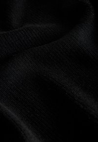 Κοντινό πλάνο μαύρου πλεκτού υφάσματος που εμφανίζει υφή και απαλά πτυχώσεις με διακριτικές αντιθέσεις φωτός και σκιάς.