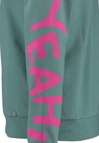 Maglietta verde a maniche lunghe realizzata in tessuto morbido, presenta una grande scritta rosa glitterata "YEAH" lungo il braccio, con un dettaglio accentato rotondo in argento all'orlo.