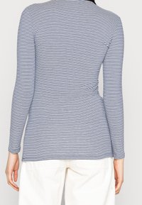 Långärmad topp i marinblå och vita ränder, smal passform, rund halsringning, mjukt tyg och sidofuktdetalj. Bärs med ljusa byxor.