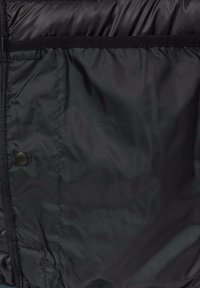 Schwarze Pufferjacke aus Stoff mit einer glatten, glänzenden Textur. Verfügt über einen Druckknopfverschluss und eine Seitentasche mit einem Klettverschluss.