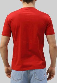 T-shirt rossa di cotone con maniche corte e scollatura a girocollo, indossata da una persona con jeans azzurri, vista da dietro.