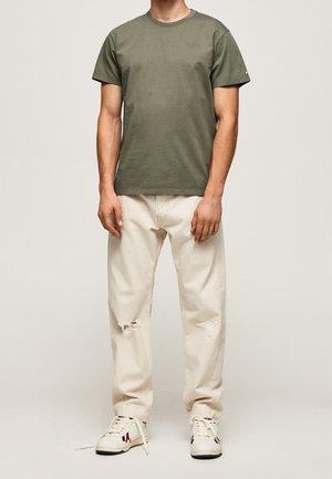 Olijfgroene t-shirt met korte mouwen en een ronde hals; gecombineerd met crèmekleurige, versleten broek en witte sneakers met rode accenten.