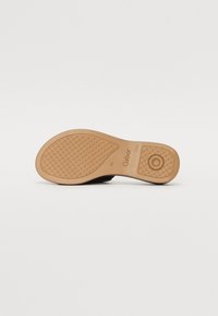 Black shoe sole with textured grip pattern, rubber material, and a tan-colored outsole featuring embossed branding details.