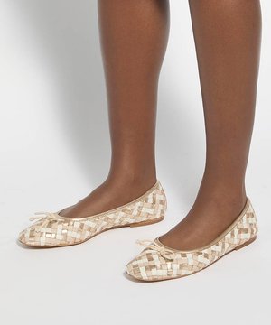 Bruine benen met beige en witte geweven ballerina's met kleine strikjes op een witte achtergrond.