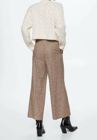 Kabelgebreide crème trui gecombineerd met hoogwaist, wijde, geruite broek in beige, bruin en rode tinten; zwarte haklaarzen.