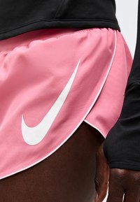 Άτομο που φοράει ροζ σορτς για τρέξιμο Nike με λευκό λογότυπο και μαύρο μακρυμάνικο μπλουζάκι, κοντινό πλάνο στο ισχίο και το χέρι.