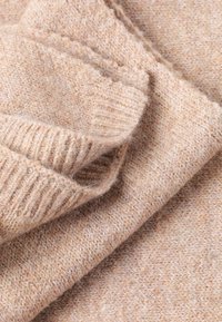 Mehakki bež volneni material z teksturiranim pletenim vzorcem; ima rebraste robove in rahlo puhasto površino. Vidni so zloženi sloji.